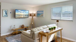 A living room with a sofa, a wooden coffee table, a TV, and artwork on the walls. - Pet-Friendly 1BR – Lemon Bay, Boats & Beaches (Englewood)