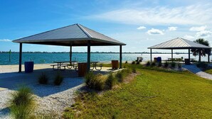 Two covered picnic areas with benches and trash bins, a grassy area, and a view of the water. - Pet-Friendly 1BR – Lemon Bay, Boats & Beaches (Englewood)