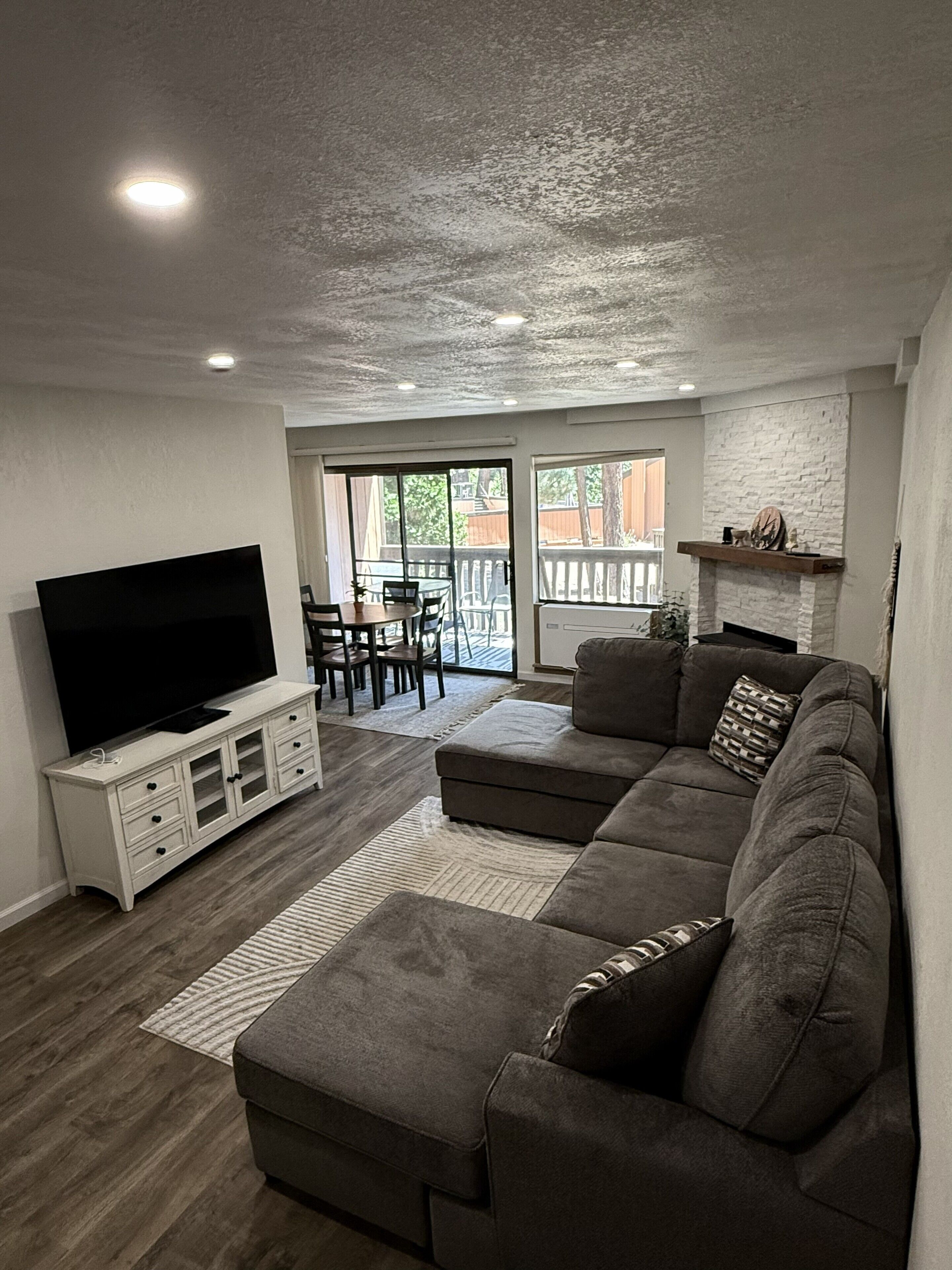 A living room with a flat-screen TV, a sectional sofa, a dining table with chairs, and a fireplace.