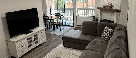 A living room with a flat-screen TV, a sectional sofa, a dining table with chairs, and a fireplace.