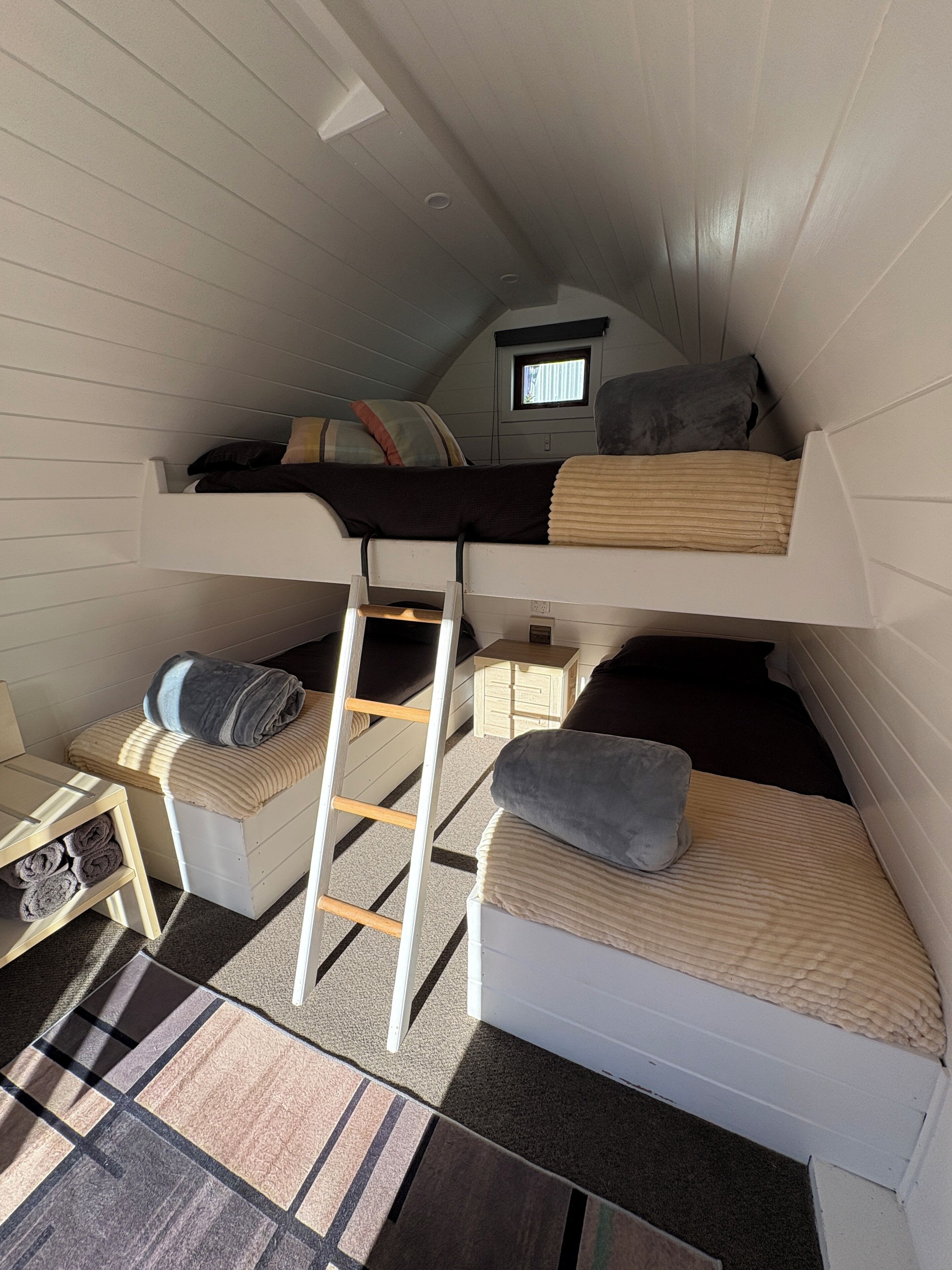 Una camera da letto in stile loft con un letto a castello, una scala, un piccolo oblò e un comodino in legno.