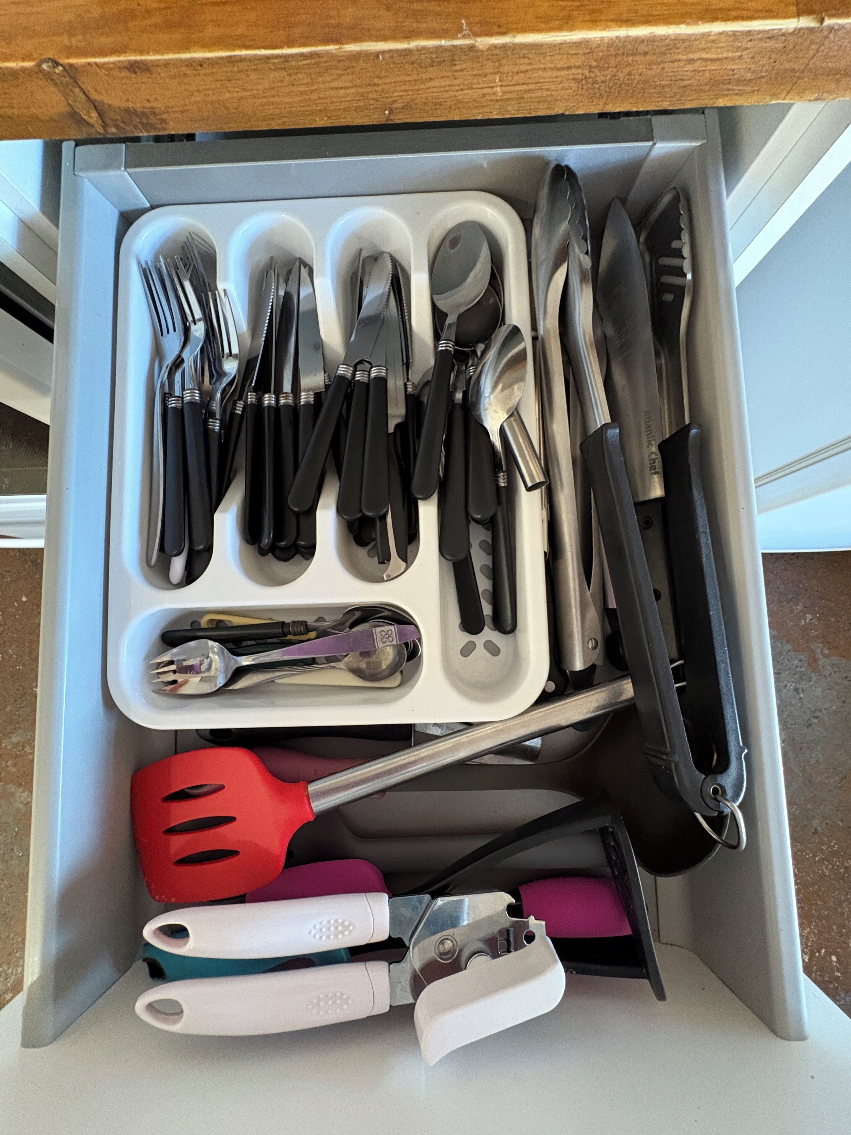 Un cajón con varios utensilios de cocina, incluyendo tenedores, cuchillos, cucharas y una espátula.