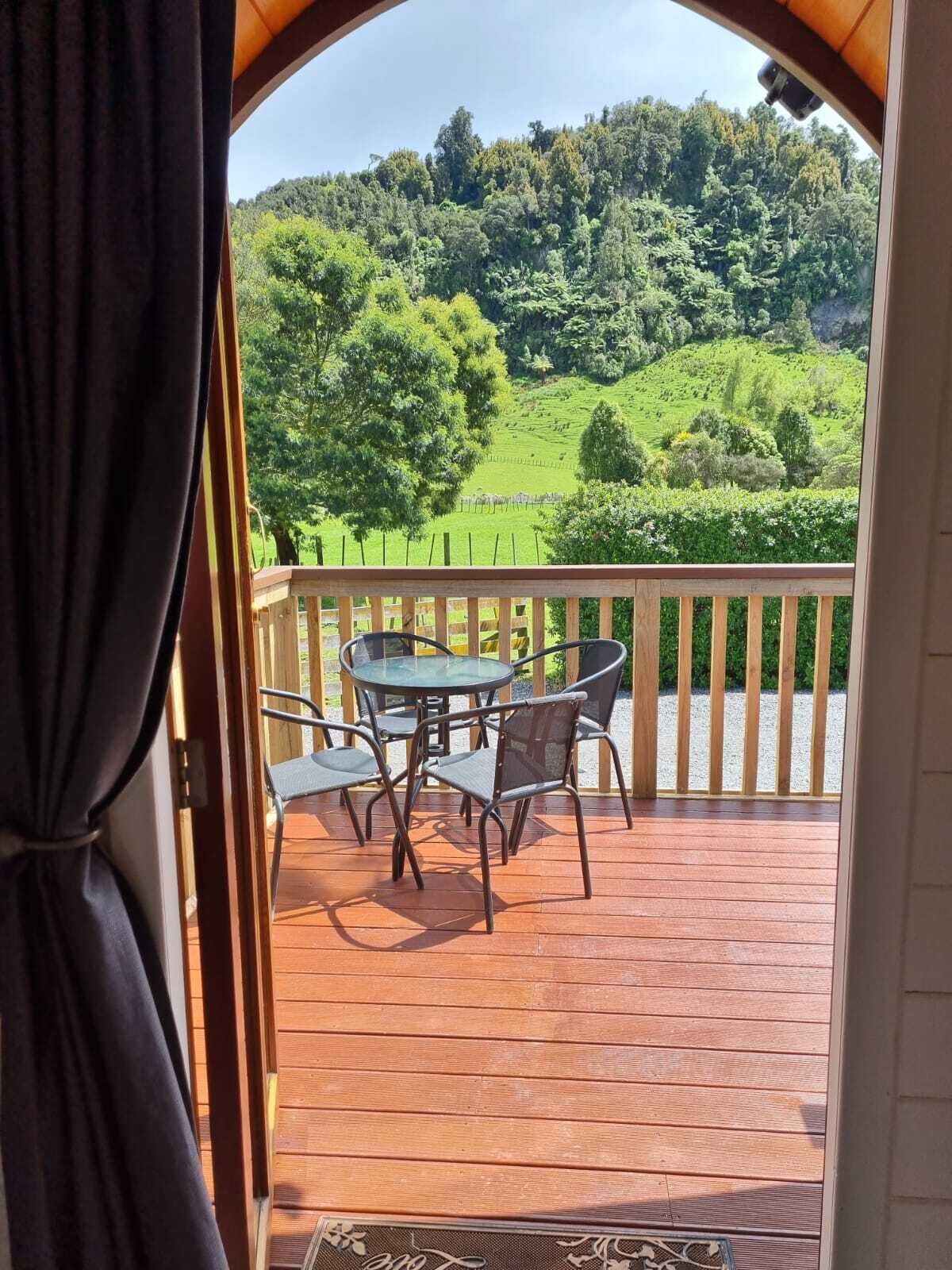Une terrasse en bois avec une table et des chaises, donnant sur un paysage verdoyant parsemé d’arbres et de collines.