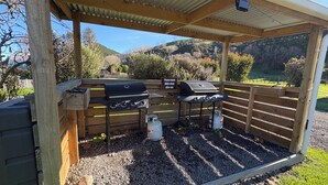 Zona de barbacoa al aire libre techada con una parrilla, tanque de gas y un letrero que indica limpiar las barbacoas después de usarlas.