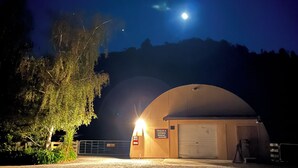 Escena nocturna con una estructura grande e iluminada, posiblemente un garaje o almacén, con un cartel que indica estacionamiento para remolques y caravanas.