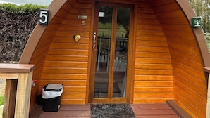 Una baita in legno con tetto curvo, un cartello con il numero '5', una porta con un vetro e un piccolo spazio esterno con posti a sedere.