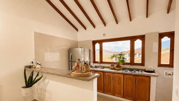 A modern kitchen with wooden cabinets, a stainless steel refrigerator, and a large window with a view.
