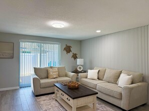 A living room with two sofas, a coffee table, a lamp, and a window with blinds. - 2BR Coastal Beach & Boating Escape (Englewood)