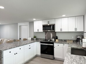 A modern kitchen with white cabinets, a stainless steel microwave, a stove, and a coffee maker. - 2BR Coastal Beach & Boating Escape (Englewood)
