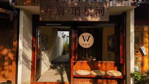 A traditional building entrance with a sign, a wooden bench, and a camera. - BX Star River Hotel (Lijiang)