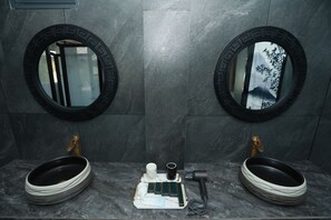 Ein Badezimmer mit zwei Waschbecken, jeweils mit einem runden Spiegel, sowie einem zentralen Waschtisch mit Handtuchhalter und Haartrockner.