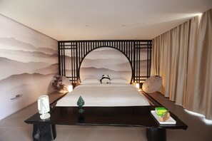 Ein Hotelzimmer mit Bett, Nachttisch, einer Wand mit Dekoration und einem Vorhang.