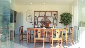 A dining area with a wooden table and chairs, a decorative wooden panel with shelves, a refrigerator, and a potted plant. - BX Star River Hotel (Lijiang)