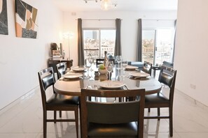 A dining area with a round table, chairs, and a view of the city through large windows. - Yacht Marina View - Modern 3 bdrs Apart M, Msida, Malta (Msida)