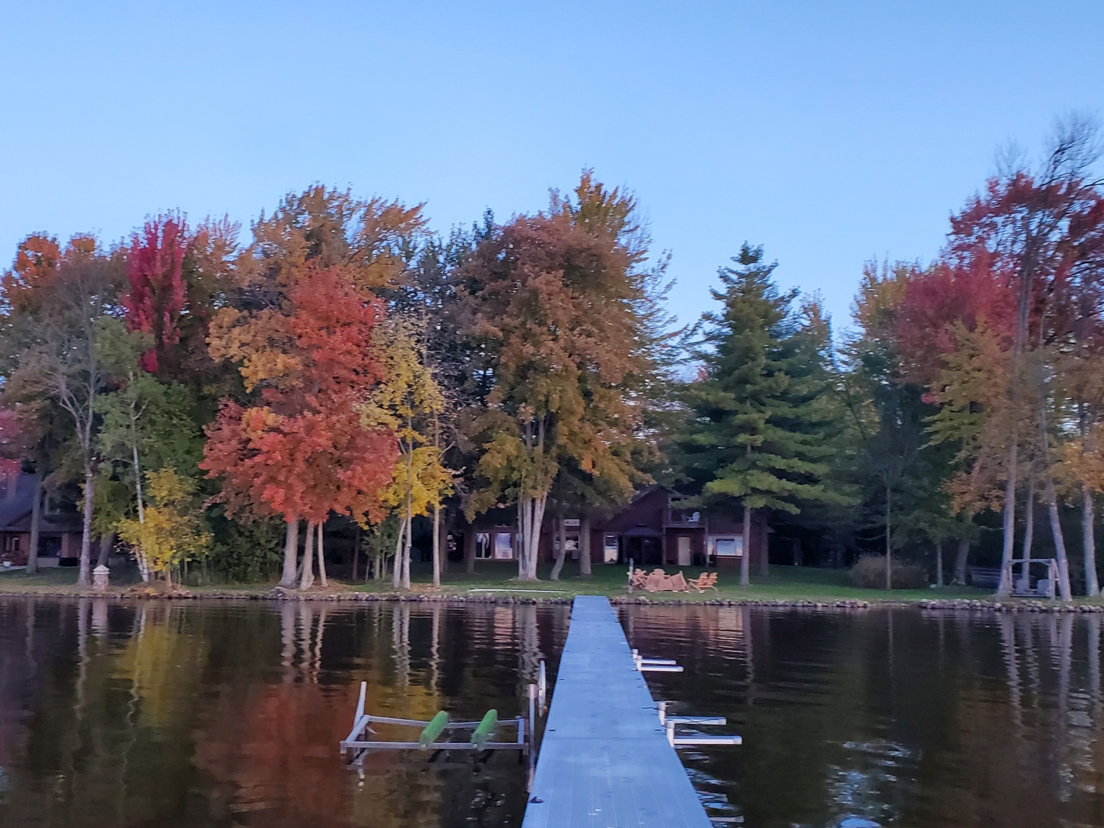 Une jetée s’avançant dans un lac paisible, entourée d’arbres aux feuilles d’automne.