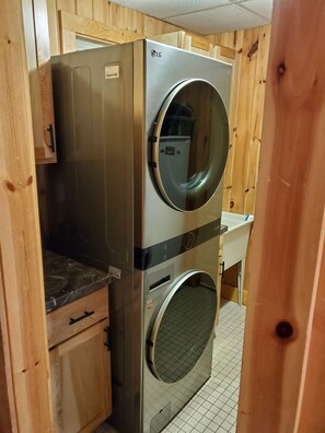 A compact laundry room with a stainless steel washer and dryer, wooden cabinetry, and a tiled floor. - Spacious 8-bedroom waterfront estate on lake Noquebay in peaceful Wausaukee (Wausaukee)