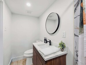 A modern bathroom with a white sink, black faucet, and a round mirror.