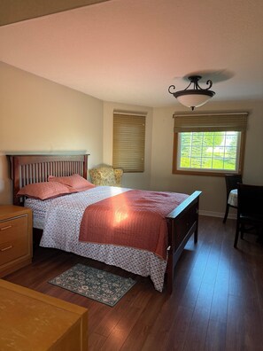 A bedroom with a wooden bed, a nightstand, a chair, a window with blinds, and a ceiling fan.