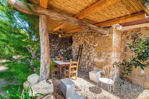 A rustic outdoor dining area with a stone wall, wooden table, chairs, and a metal chair. - Villa Fontanelle in Ugento With Garden, Ugento, Italy (Ugento)