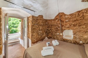 Une pièce avec un mur en pierre rustique, un lit doté d’un matelas matelassé et une petite fenêtre.