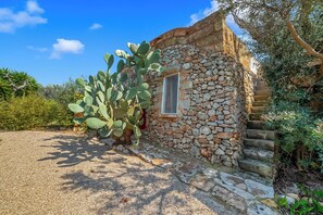 Un bâtiment en pierre doté d’une fenêtre, entouré de cactus et d’oliviers.