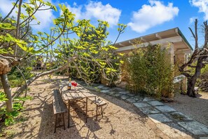 Un jardín con una mesa y sillas, una estructura cubierta y un sendero de piedra.