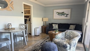 Una sala de estar con sofá, reposapiés, mesa de centro y un comedor con sillas y una mesa.