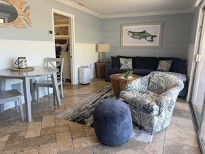 Ein Wohnzimmer mit einer Couch, einem Hocker, einem Couchtisch und einem Essbereich mit Stühlen und einem Tisch.