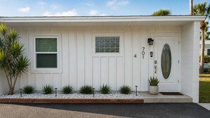 Una casa de una sola planta con fachada blanca, una puerta principal con panel de vidrio y un buzón.