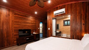 Una habitación con paredes de madera, una cama, un televisor, un baño con espejo y un equipo de aire acondicionado.