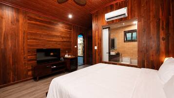 A room with wooden walls, a bed, a TV, a bathroom with a mirror, and an air conditioning unit.