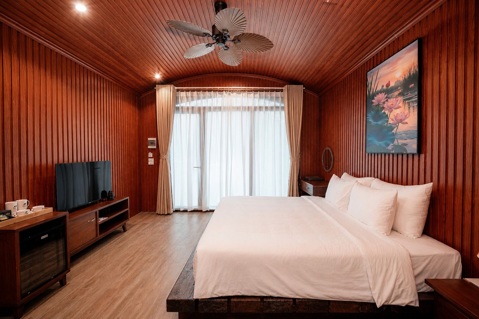 Hotellihuone, jossa on puinen katto, sänky, televisio ja kukkakuva.