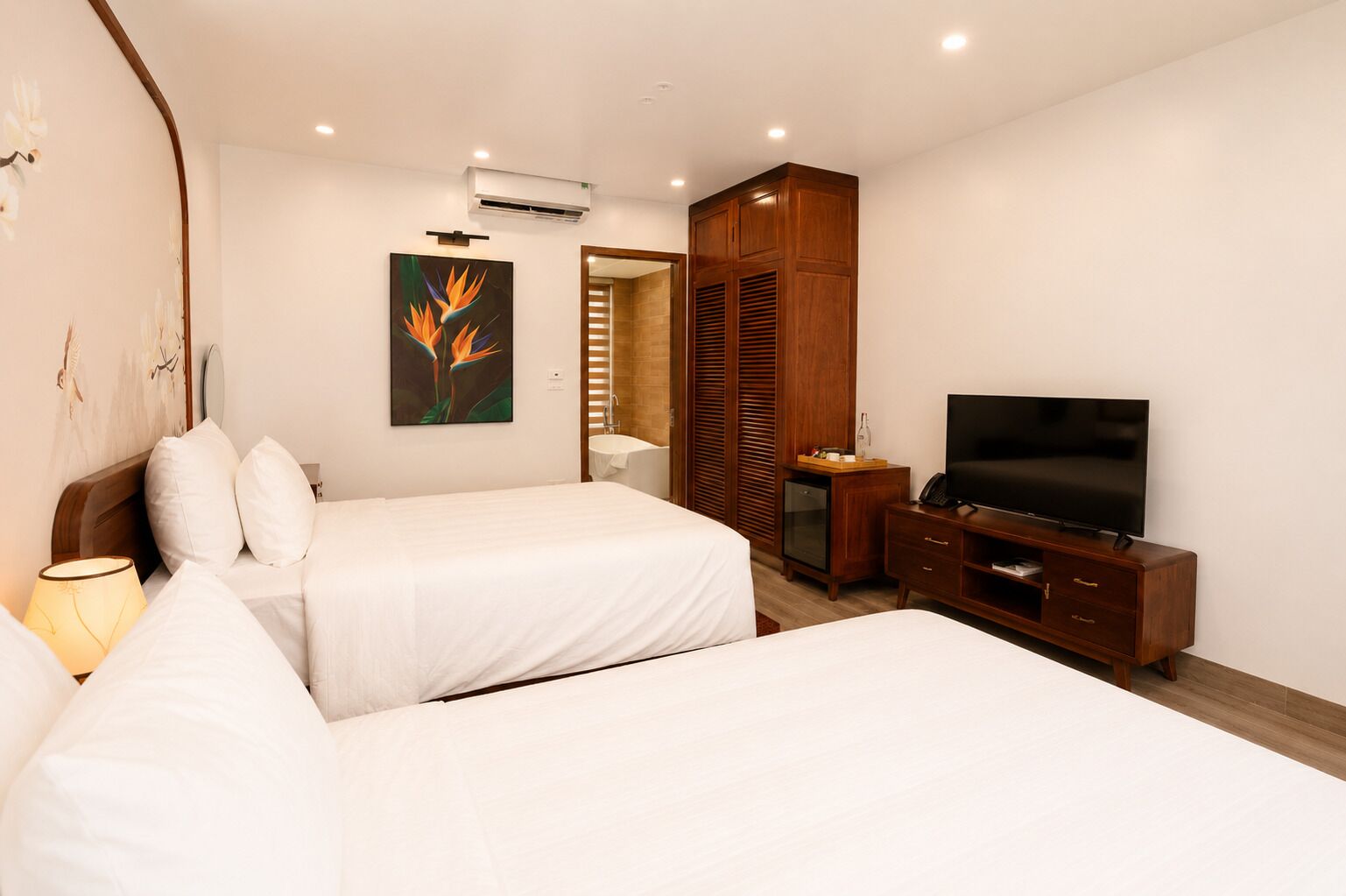 A hotel room with two beds, a TV, a minibar, and a wooden wardrobe.