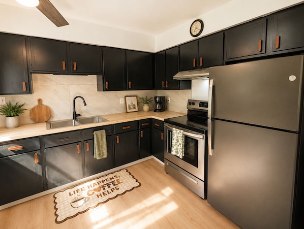 Una cocina moderna con armarios negros, electrodomésticos de acero inoxidable y encimera de madera.