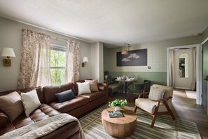 A living room with a brown leather sofa, a wooden coffee table, and a dining area with a green table and chairs. - Private Retreat:: Hot Tub, Sauna & Fire Pit (Logan)
