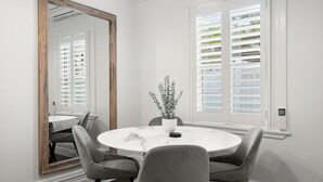 Ein Essbereich mit einem runden Tisch, vier Stühlen, einem Blumentopf, einem großen Spiegel und einem Fenster mit Fensterläden.