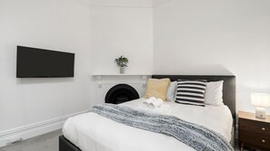 Ein Schlafzimmer mit Bett, Flachbildfernseher, Kamin und Nachttisch mit Lampe.