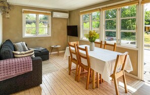 Une pièce comprenant une table à manger, des chaises, un canapé, un téléviseur et de grandes fenêtres.