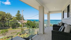 A balcony with a view of the ocean, outdoor furniture, and a glass railing.