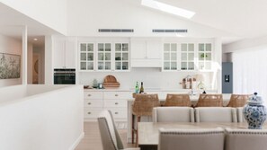 Een moderne keuken met witte kasten, een centraal eiland en een eethoek met rieten stoelen.