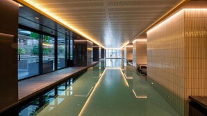 Piscina interior moderna com barreira de vidro, teto com padrão de grade e vista do exterior por grandes janelas.