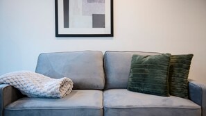 Un canapé gris avec un plaid blanc et deux coussins verts.