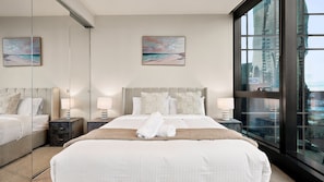 Une chambre d’hôtel moderne avec un grand lit, deux tables de chevet, un miroir et une vue sur la ville.
