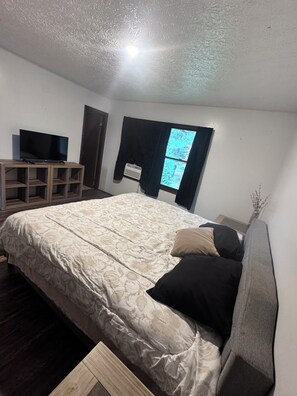 Un dormitorio con una cama, un televisor sobre un mueble de madera, una ventana con cortinas y un radiador.