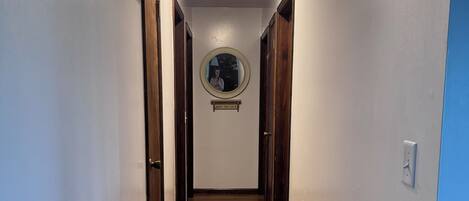 A hallway with wooden flooring, a round mirror on the wall, and a ceiling light.