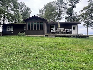 A two-story cabin with a deck, large windows, and outdoor seating.