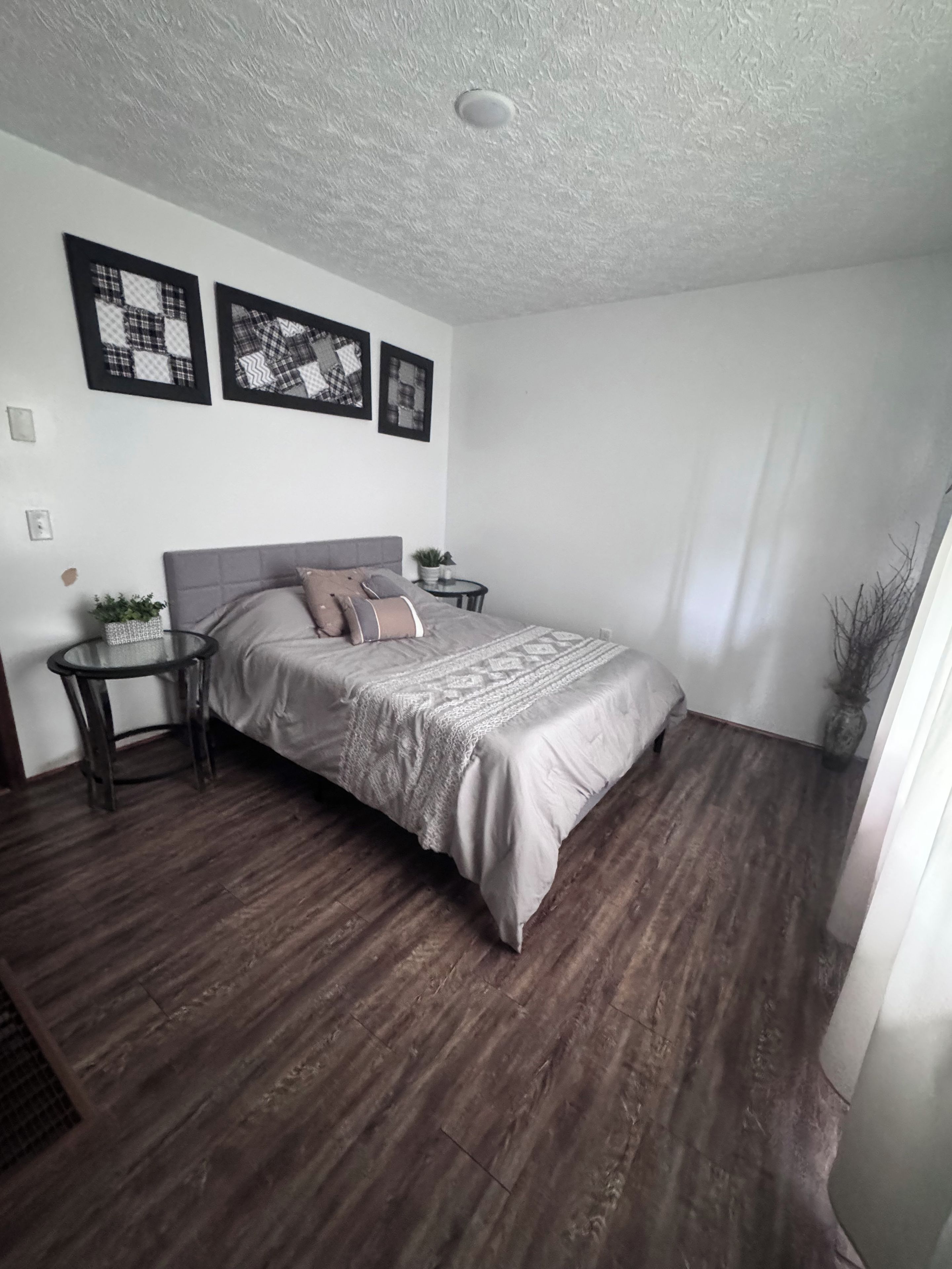 A bedroom with a bed, a nightstand, a small table, and a potted plant.