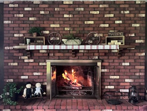 A brick fireplace with a fire, shelves above with decorative items, and a small table with two dolls.