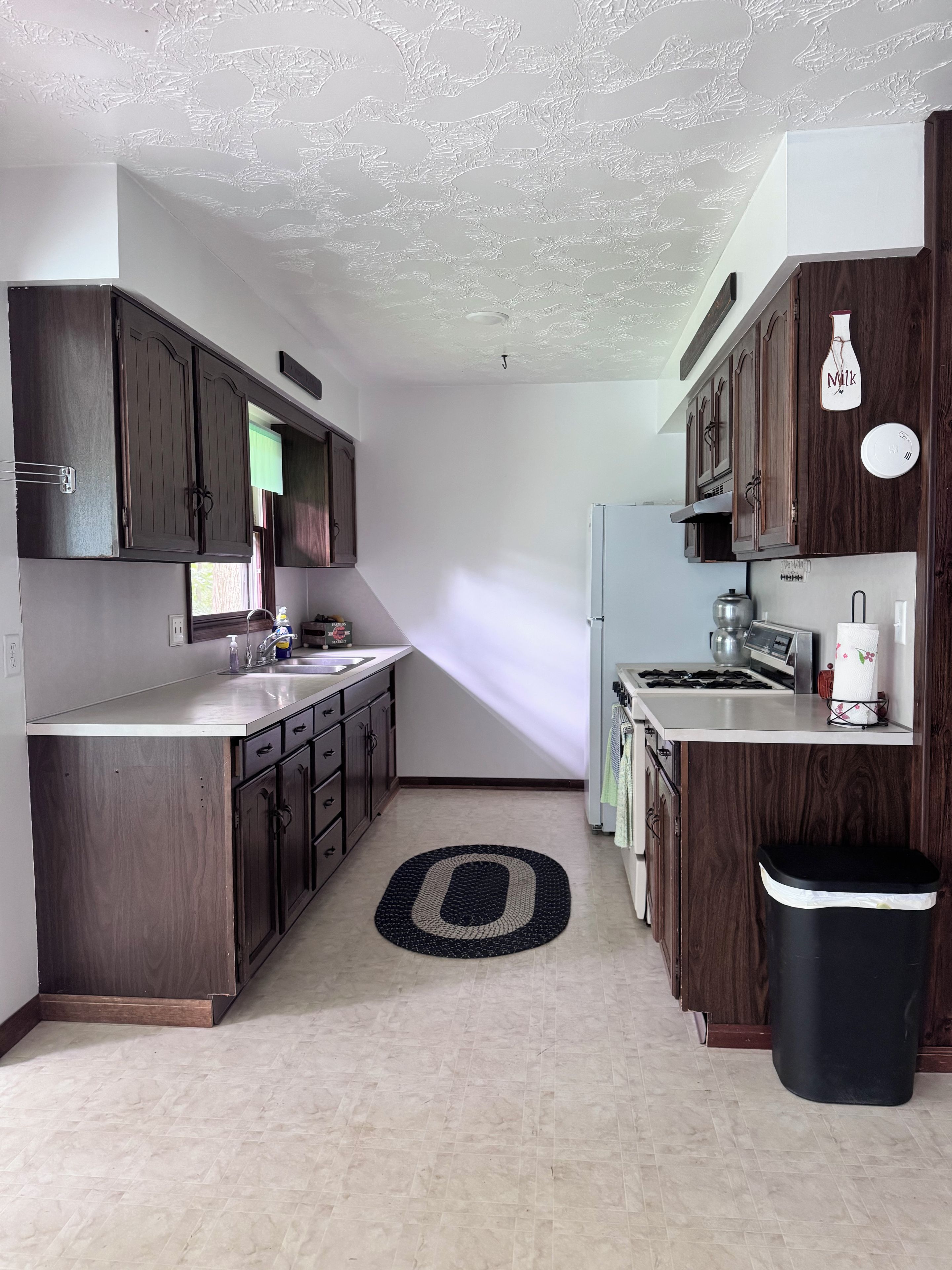 A modern kitchen with dark wood cabinets, a stainless steel sink, and a black trash bin.