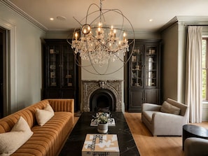 A living room with a fireplace, dark wood cabinets, a brown sofa, a grey armchair, and a black marble coffee table.